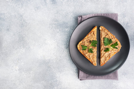 Sandwiches crispy toast and chicken liver pate with parsley leaves on a black plate on a gray...