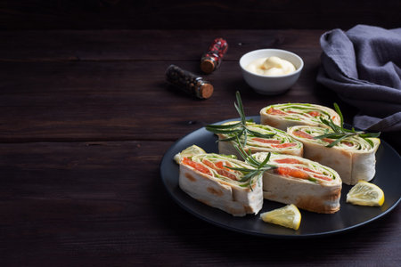 Rolls of thin pita bread and red salted salmon with lettuce leaves on a black ceramic plate, dark...
