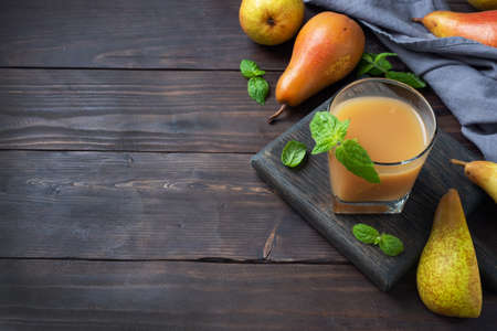 Natural pear juice in a glass cup. Juicy ripe conferences pears and mint leaves top view copy space Dark rustic wooden background.の写真素材