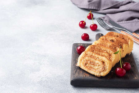 Dessert sponge roll with chocolate cream with cherries on a wooden cutting Board. Copy spaceの写真素材