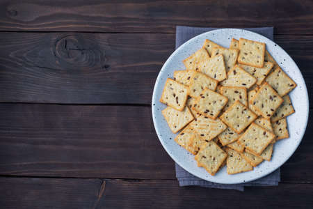 Delicious healthy cookies crackers with flax seeds and sesame seeds on a plate. Background of a healthy snack food, dark rustic wooden table. Copy spaceの写真素材