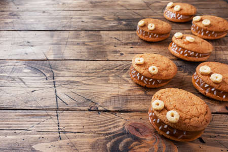 Cookies with cream paste in the shape of monsters for Halloween celebration. Funny homemade faces made of oatmeal cookies and boiled condensed milk copy spaceの写真素材