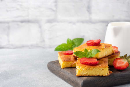 Cottage cheese casserole with strawberries and mint. Delicious homemade dessert made of curd and fresh berries with cream Gray concrete background, copy spaceの写真素材