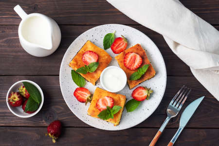 Cottage cheese casserole with strawberries and mint. Delicious homemade dessert made of curd and fresh berries with cream dark wooden background, copy spaceの写真素材