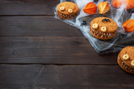 Cookies with cream paste in the shape of monsters for Halloween celebration. Funny homemade faces made of oatmeal cookies and boiled condensed milk copy spaceの写真素材