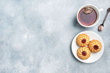 Kurabye shortbread cookies with berry jam in a plate and a cup of tea. Delicious dessert, gray concrete background with copy spaceの写真素材