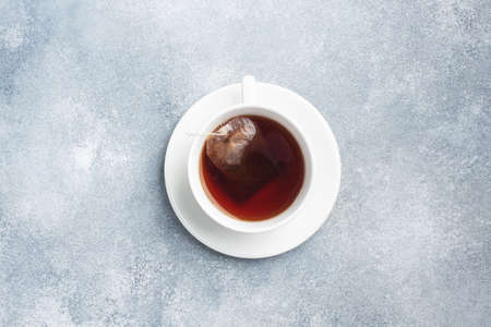 A cup of black tea bags in a white cup with a saucer. Gray concrete background with a copy of the spaceの写真素材