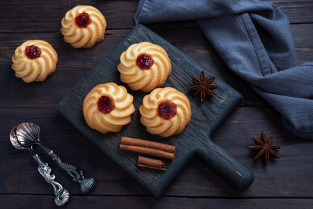 Kurabye shortbread cookies with berry jam in a black plate. Delicious dessert, dark wooden...