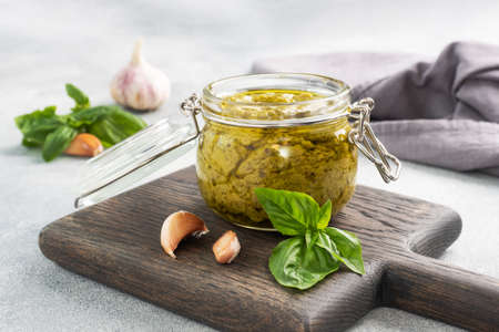 Pesto sauce in a glass jar, fresh basil leaves and garlic, copy spaceの写真素材