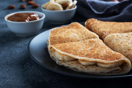 Pancakes with chocolate banana filling. Delicious breakfast of pancakes envelopes on a plate, dark concrete backgroundの写真素材