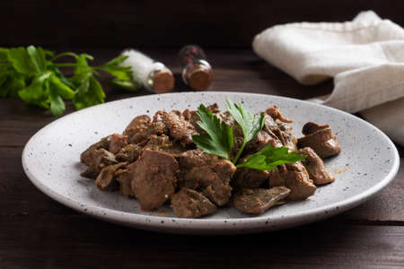 Fried or baked chicken liver with onion and sauce, green parsley leaves on a plate. Meat dish enriched with ironの写真素材