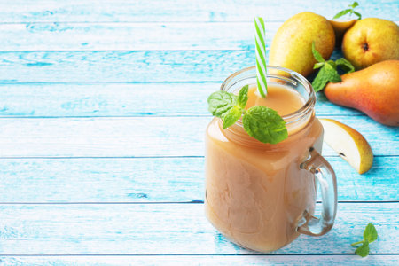 Natural pear juice in a glass cup. Juicy ripe conferences pears and mint leaves top view copy space Bright blue background.の写真素材
