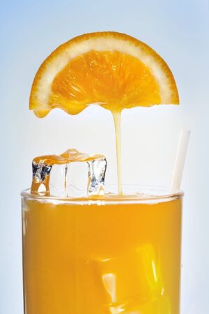 Orange juice is flowing in a glass with iceの写真素材