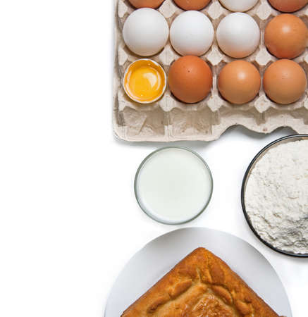 Raw eggs, glass of milk, flour and baked good isolated on whiteの写真素材