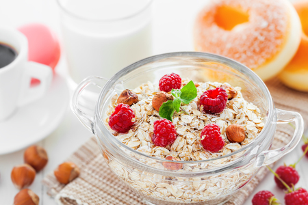 Healthy food. Oatmeal muesli with raspberry and hazelnut, coffee and doughnut on white table.の写真素材