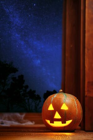 Halloween pumpkin head jack o lantern near window, night sky full of stars on backgroundの写真素材