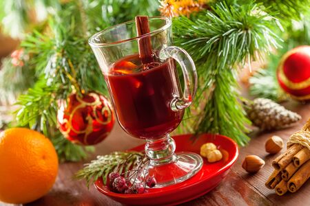Holiday winter hot drink. Mulled wine with fruits and spices by Christmas tree with decorations.の写真素材