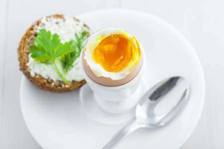Perfect soft boiled egg, open bread sandwich with butter and cup of coffee on a table. Traditional...