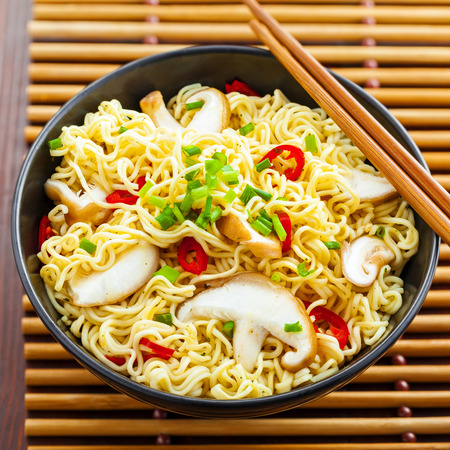 Instant noodles with shiitake mushrooms, pepper and onion in a bowl, Asian meal on a table, top viewの写真素材