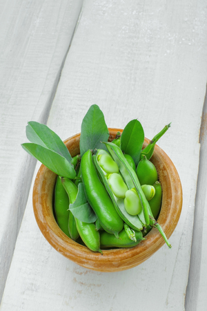 Fresh green broad beans in a bowl. Fresh raw vegetables on a wooden table. Ingredients healthy vegetarian food. Top view.の写真素材