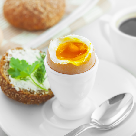 Perfect soft boiled egg, open bread sandwich with butter and cup of coffee on a table. Traditional food for healthy breakfast.の写真素材