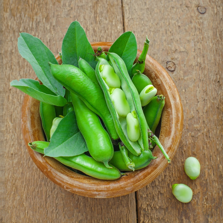 Fresh green broad beans in a bowl. Fresh raw vegetables on a wooden table. Ingredients healthy vegetarian food. Top view.の写真素材