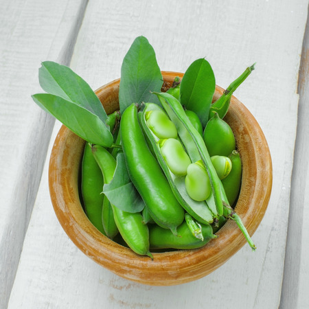 Fresh green broad beans in a bowl. Fresh raw vegetables on a wooden table. Ingredients healthy vegetarian food. Top view.の写真素材