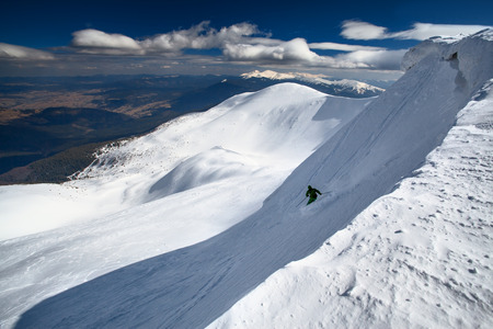 Freeride ski in deep powder snow of Carpathian mountains. Skier skiing downhill in winter mountains. Hoverla peak on background.の写真素材