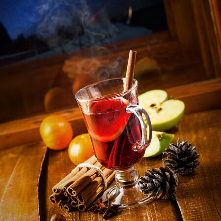 Winter holiday hot alcohol drink on a table. Mulled wine with fruits and spices by window, winter landscape with sky full of stars on background.の写真素材