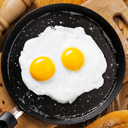 Two fried eggs in a frying pan cooked for breakfast. Delicious international meal on a table. Homemade food, top view.の写真素材