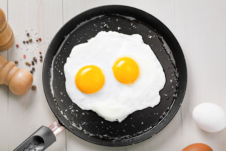 Fried eggs for delicious healthy easy breakfast on a table. Fresh homemade meal on a frying pan. Traditional breakfast food. International cuisine food.  Top view.の写真素材