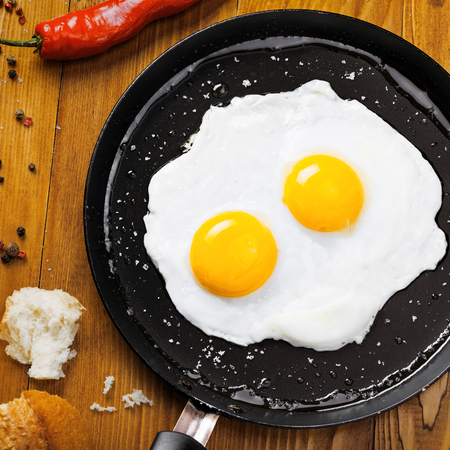 Traditional healthy easy quick breakfast meal made of two fried eggs served on a frying pan. International simple food, top view.の写真素材