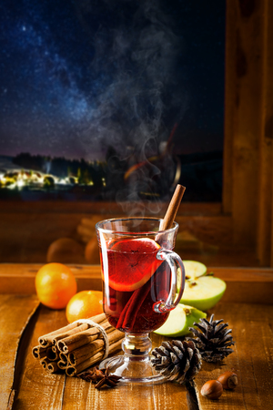 Mulled wine for Christmas Eve celebration party on a table. Traditional winter Christmas drink near the window, winter landscape with sky full of stars on background.の写真素材