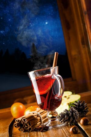 Winter holiday hot alcohol drink on a table. Mulled wine with fruits and spices by window, winter landscape with sky full of stars on background.の写真素材