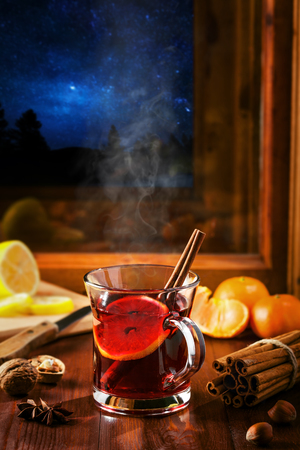 Glass of mulled wine on a table at window, winter night starry landscape on background. Traditional Christmas hot drink.の写真素材