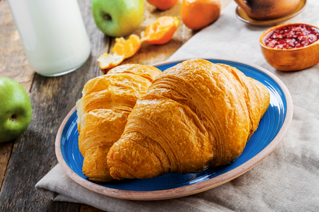 Classic French food for healthy breakfast. Plate of fresh croissants, fruit jam and milk on a rustic wooden table.の写真素材