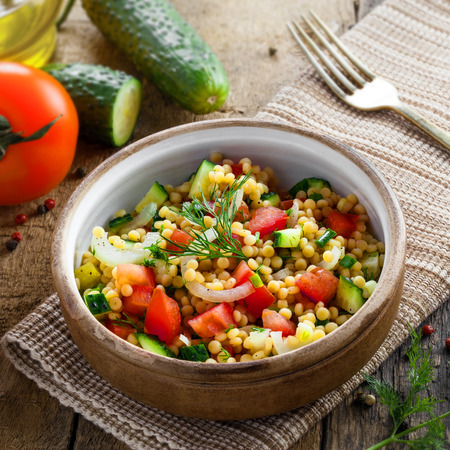 Traditional Israeli healthy meal Ptitim with tomatoes, cucumber and onion for delicious healthy breakfast. Classic Moroccan couscous with vegetables. Top view.の写真素材