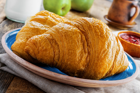 Delicious croissants with jam, milk, fresh fruits and milk for healthy breakfast. Traditional French food on a rustic wooden table. Close-up shot.の写真素材