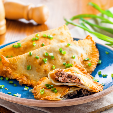 Traditional Romania, Ukrainian, Russian and Tatar food cheburek with meat and spring onion. National east meal. Meat pastry on a blue plate.の写真素材