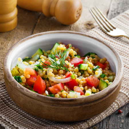 Traditional Israeli healthy meal Ptitim with tomatoes, cucumber and onion for delicious healthy breakfast. Classic Moroccan couscous with vegetables.の写真素材