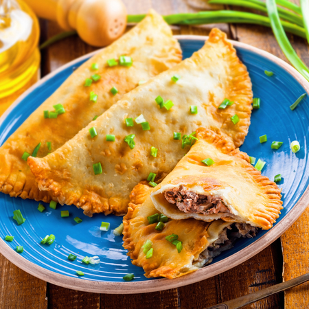 Traditional Romania, Ukrainian, Russian and Tatar food cheburek with meat and spring onion. National east meal. Meat pastry on a blue plate. Top view.の写真素材