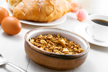 Delicious healthy breakfast with oatmeal granola, coffee and croissant on a white wooden table. Traditional healthy food.の写真素材