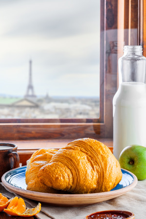 Traditional French breakfast with croissants, fruit jam and milk on a table. Delicious European healthy meal, Paris landscape behind a window on a background. Food tour in France.の写真素材