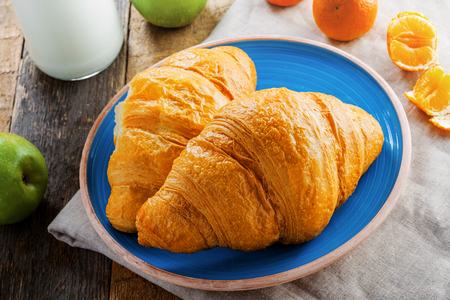 Delicious croissants with jam, milk, fresh fruits and milk for healthy breakfast. Traditional French food on a rustic wooden table. Top view.の写真素材