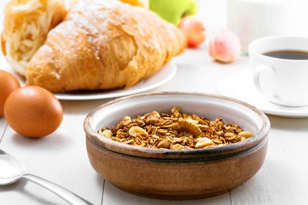 Oatmeal muesli with nuts, croissants, fruits, milk and coffee for delicious breakfast. Traditional healthy meal for breakfast on a table. Close-up.の写真素材