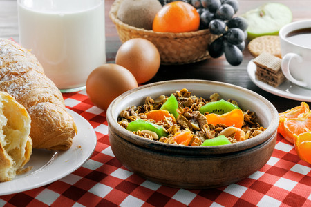 Delicious healthy breakfast with oatmeal granola, fruits, eggs, coffee and croissant on a brown wooden table. Traditional healthy food.の写真素材