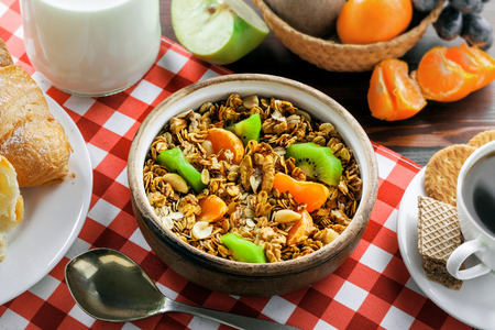 Healthy food for breakfast on a brown wooden table. Oatmeal granola with nuts, coffee, croissants, eggs, milk and fruits for delicious healthy meal. Top view.の写真素材
