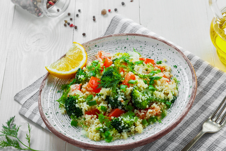 Plate with couscous and vegetables on a rustic white wooden table. Traditional eastern healthy meal made of couscous, broccoli, tomato, pepper, onion and dill. Top view.の写真素材