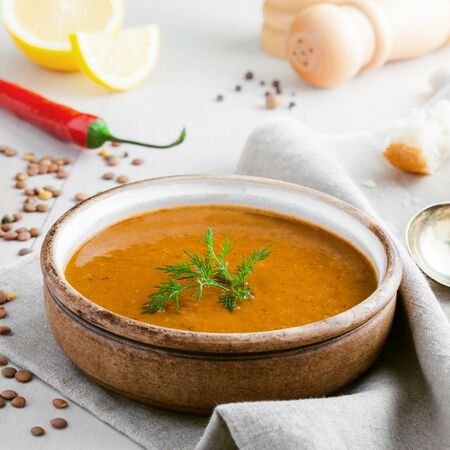 Bowl of delicious lentil soup with bread, lemon slice and spoon on a white wooden table. Traditional healthy vegetarian food.の写真素材