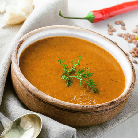 Soup made of lentil and vegetables in a rustic bowl with piece of bread on a canvas tablecloth. Delicious healthy vegetarian food on a white wooden table.の写真素材